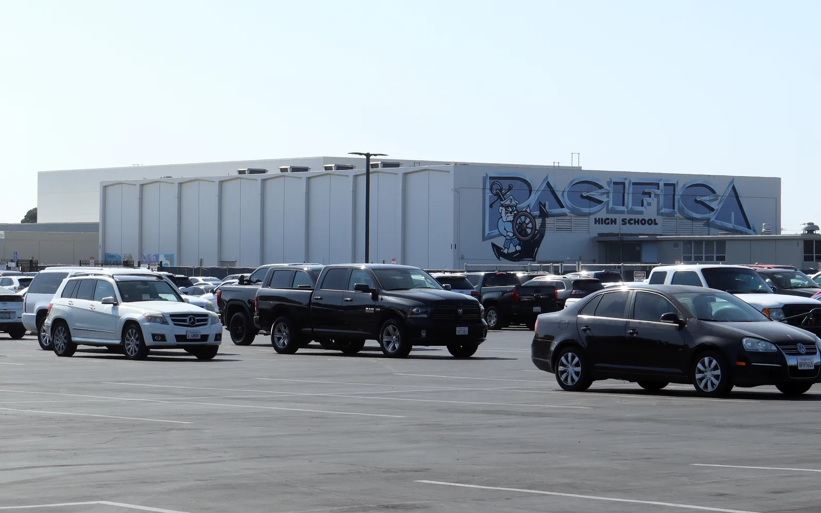 Modern school gymnasium and parking lot with athletic facility under clear blue sky